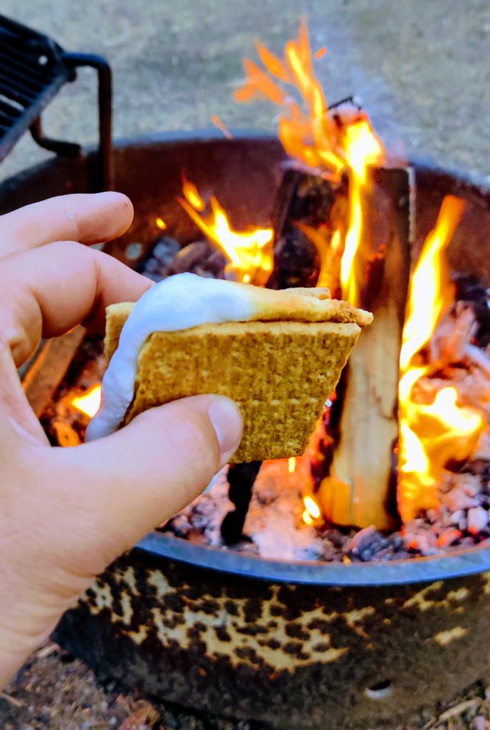 A hand holding a smore over a fire pit before summiting Longs Peak