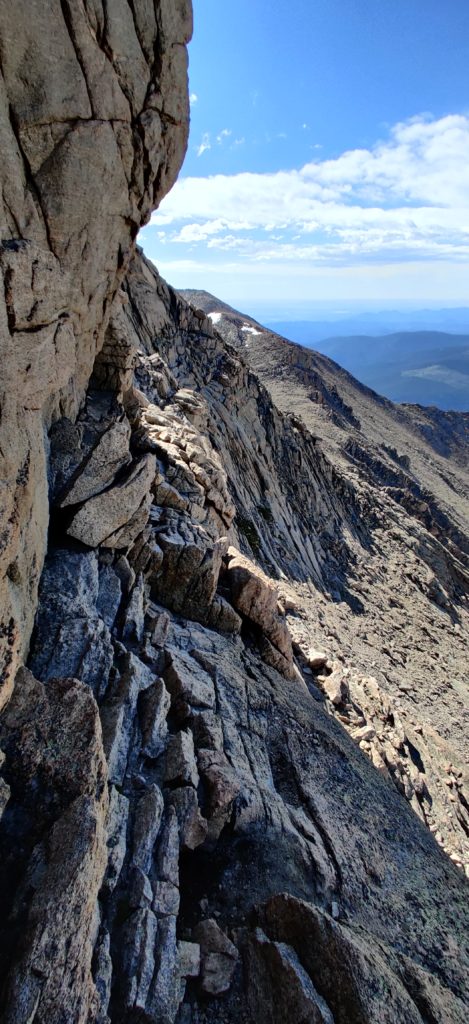 A steep dropoff on a rocky moutain  side with yellow markings indicating the trial