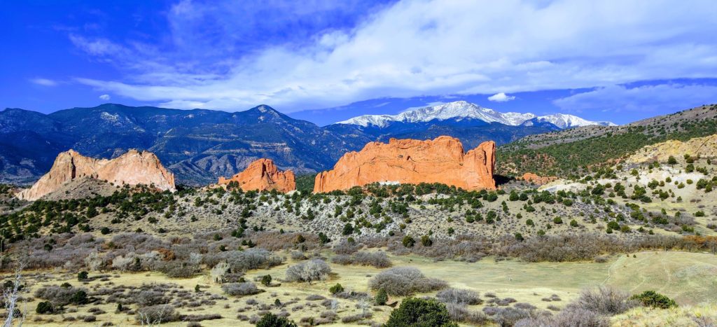 A snow-capped Pikes Peak mountain rises behind the massive, red Garden of the Gods rocks