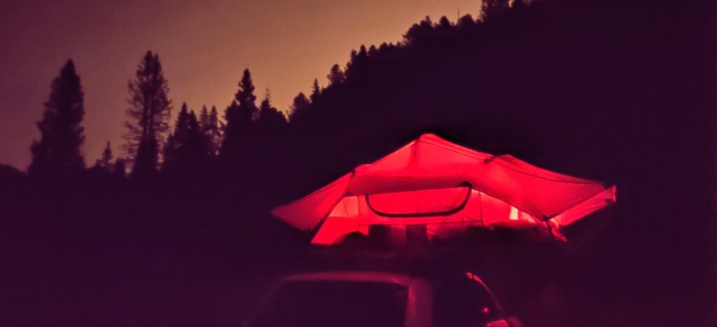 A tent on top of a car with trees sillhouetted in the background