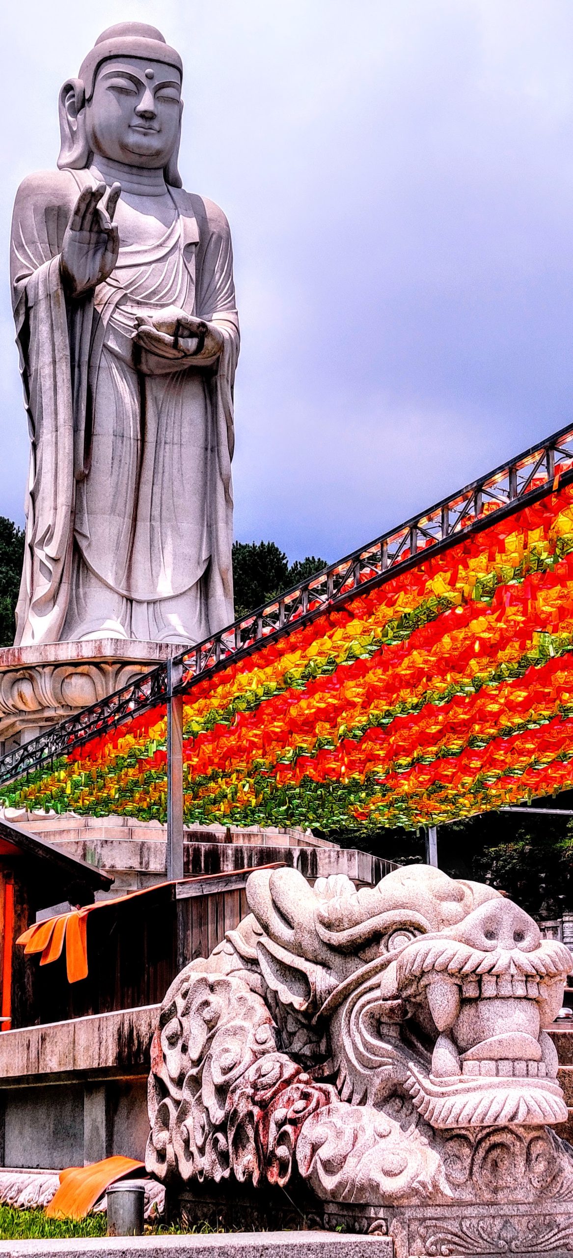 a larger-than-life buddha sculpture in south korea with a stone lion and many red and orange lanterns Donghwasa Daegu