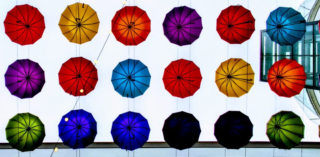 Colorful umbrellas suspended between buildings set against a rainy sky photographed from underneath 