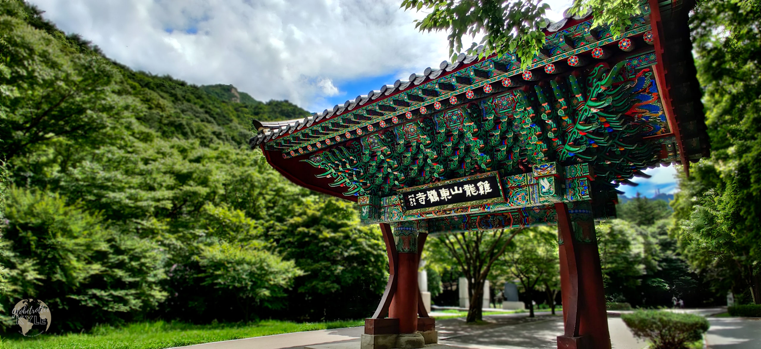 a brightly colored buddhist one pillar gate stands in a lush mountain valley leading to a temple in south korea