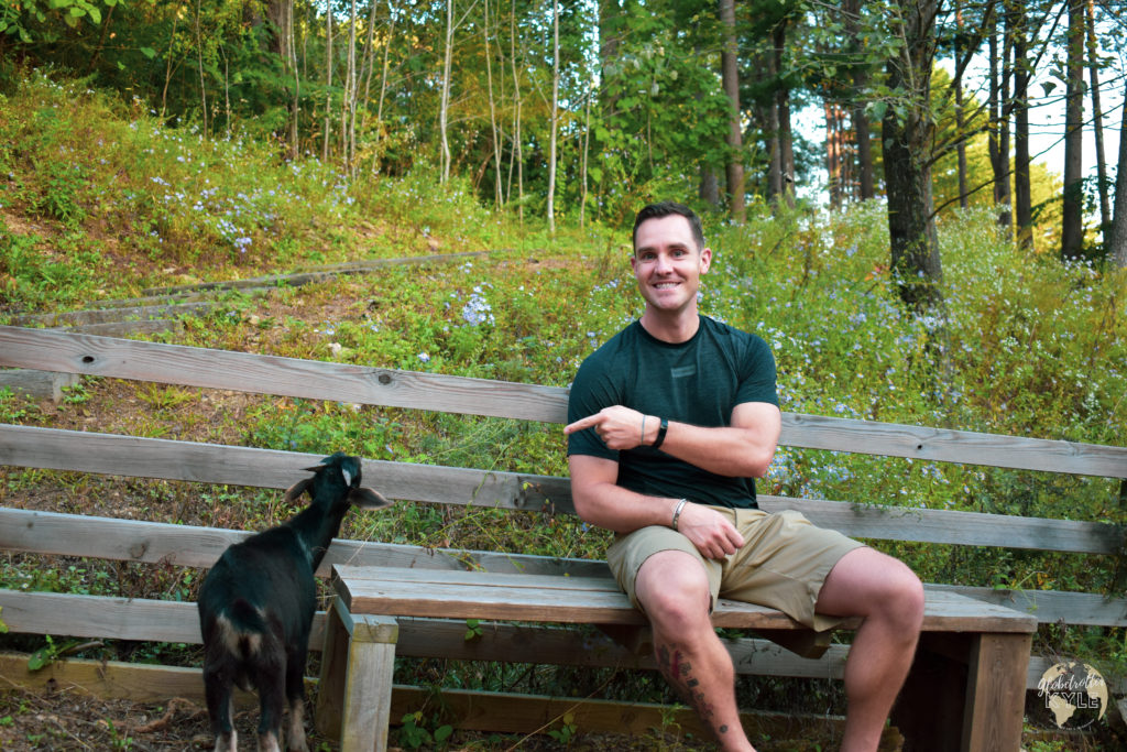 A man sitting and smiling on a bench with a goat