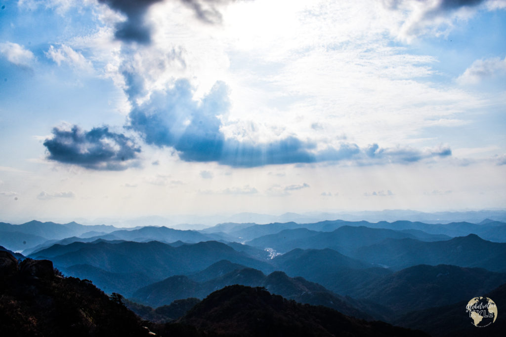 a mountain range with clouds above it and the sun shining through in streaks in south korea