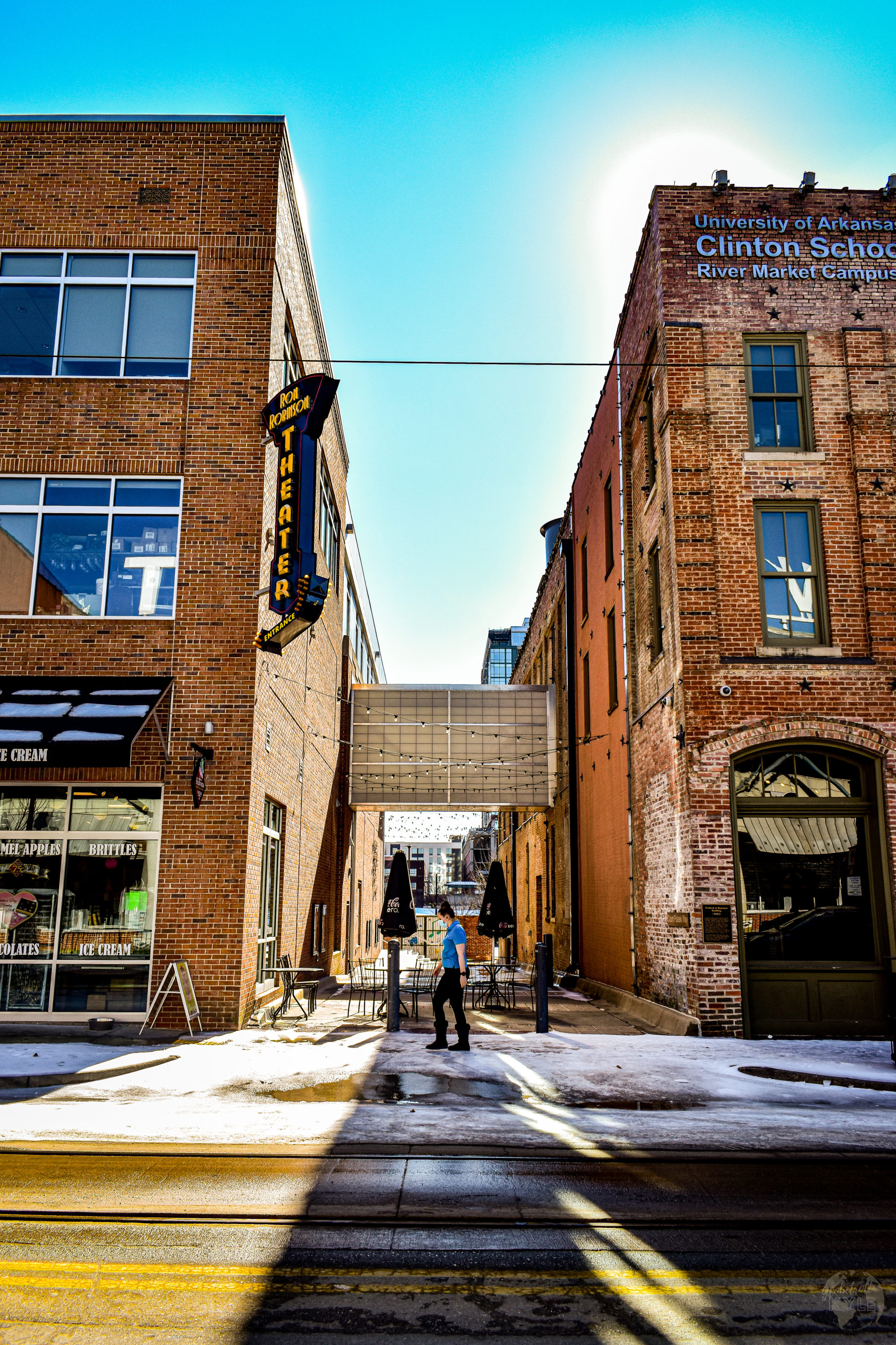 a woman walks perpendicular to an ally in between two industrial buildings in the river market district arkansas