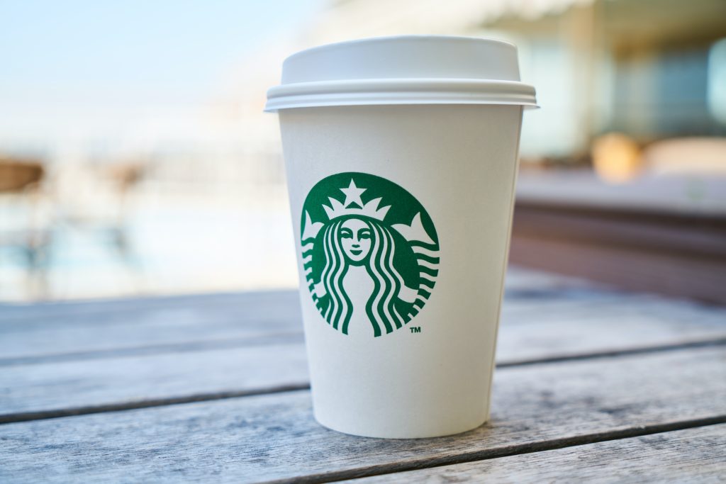A starbucks coffee cup to go on a picnic bench