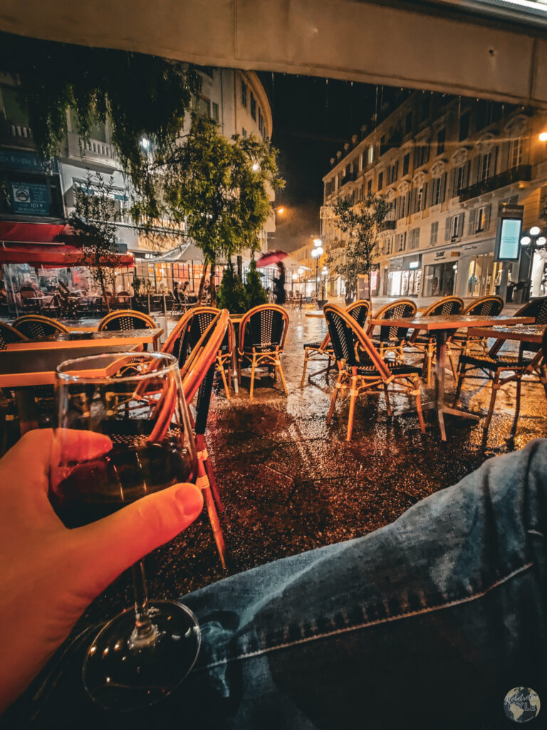 a point of view of a person holding a glass of wine at a cafe in Nice, France while it rains