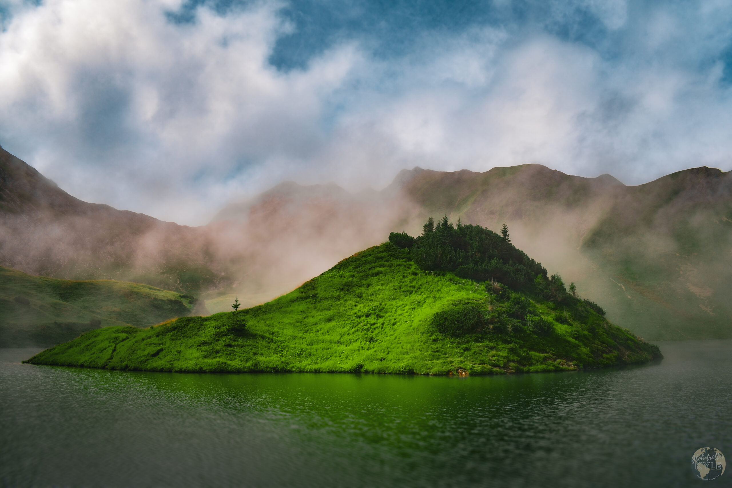 a green island surrounded by water with a mountain range behind it found by hiking in germany