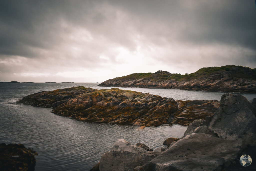 Rocky land masses in the sea with dark clouds overhead seen while hiking the Lofoten Islands