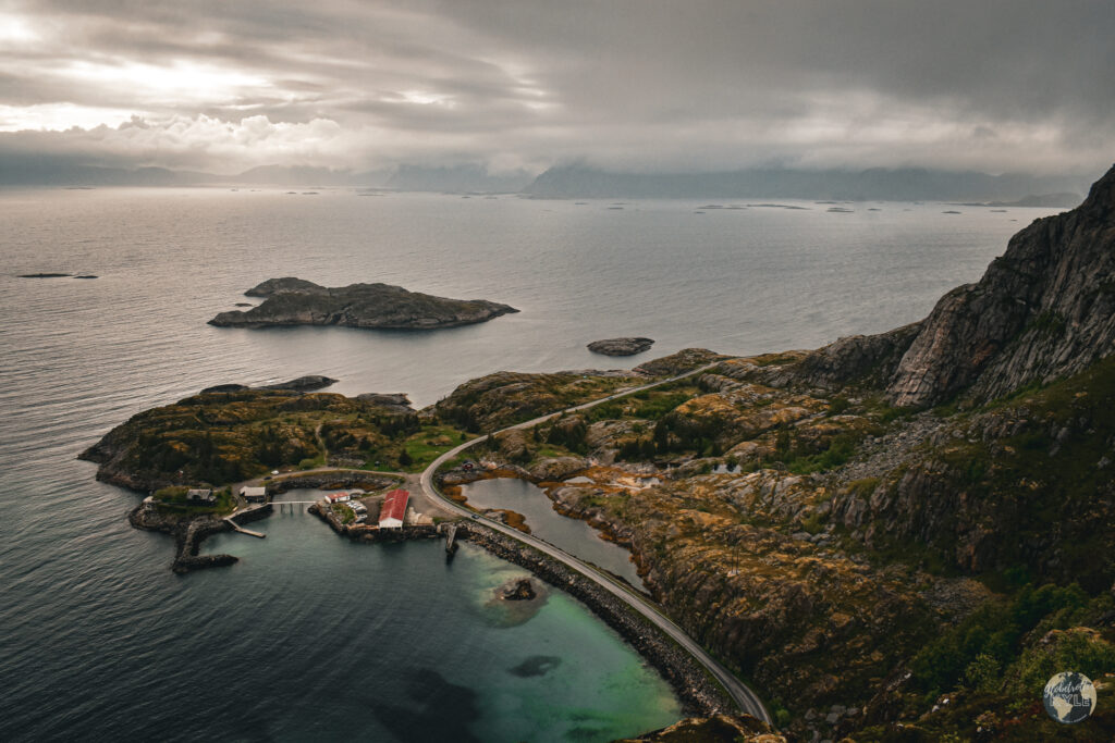 A road winds along a rocky coastline seen from Festvågtind while hiking the Lofoten Islands