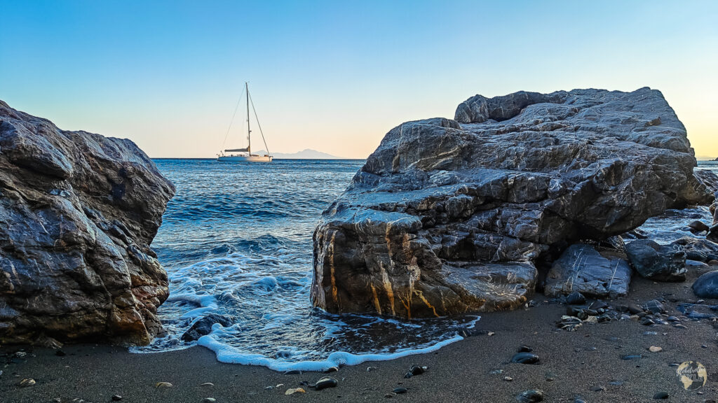 Water washes between two rocks with a yacht in the background on the island of Kos Greece