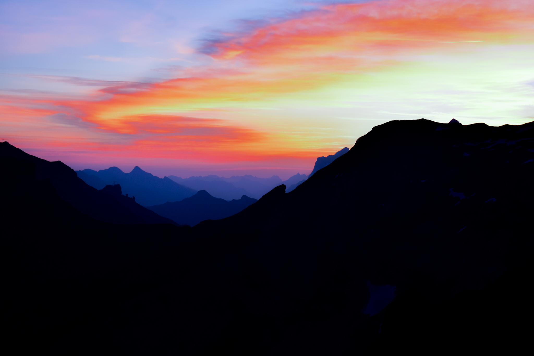 a sunrise over the swiss alps that shows red, orange, and yellows in the sky while the mountains are silhouetted and appear purple and blue. 