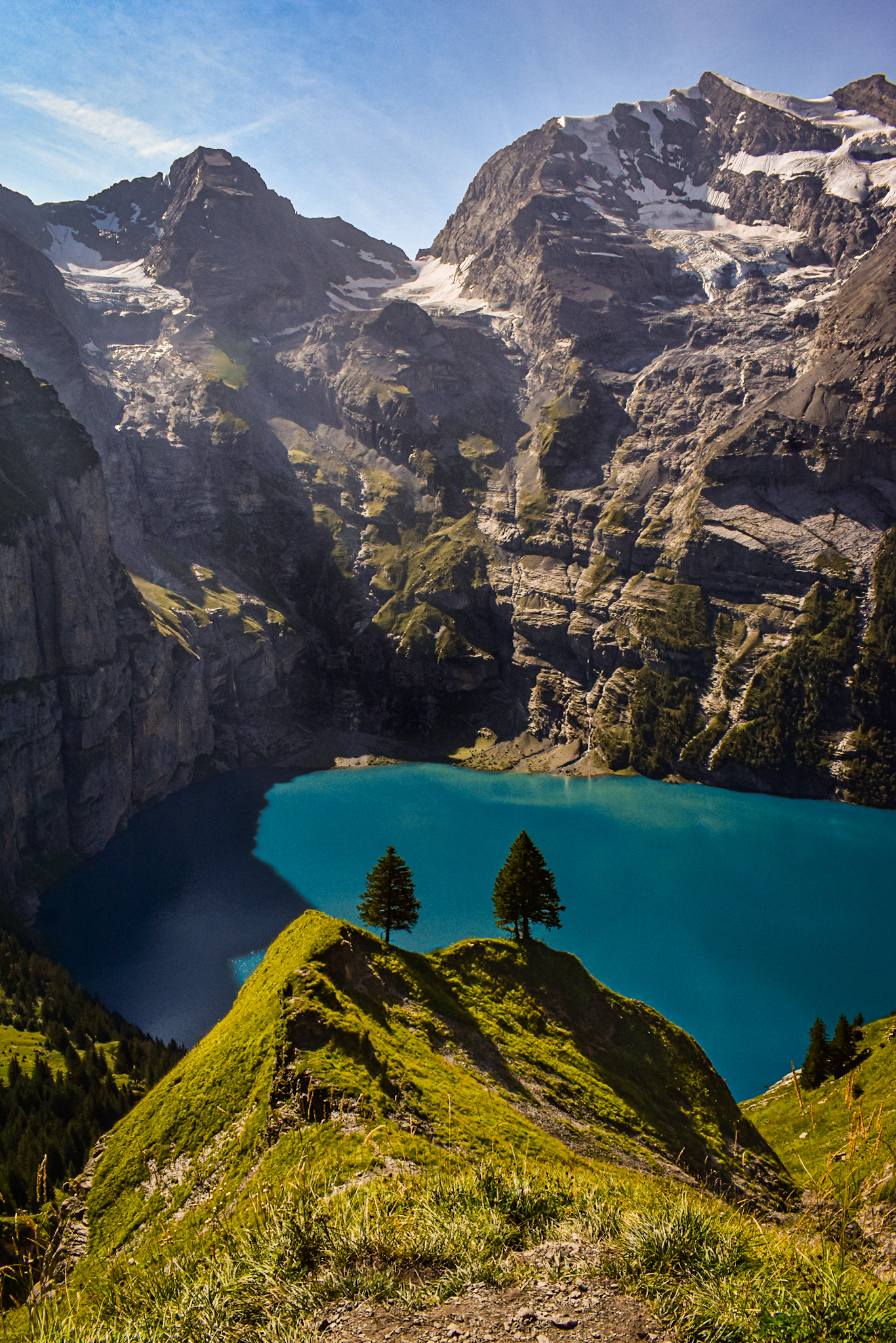 two pine trees in front of the blue waters of Lake Oeschinensee in the Swiss Alps, a sight commonly seen when doing a hut to hut hiking in Switzerland