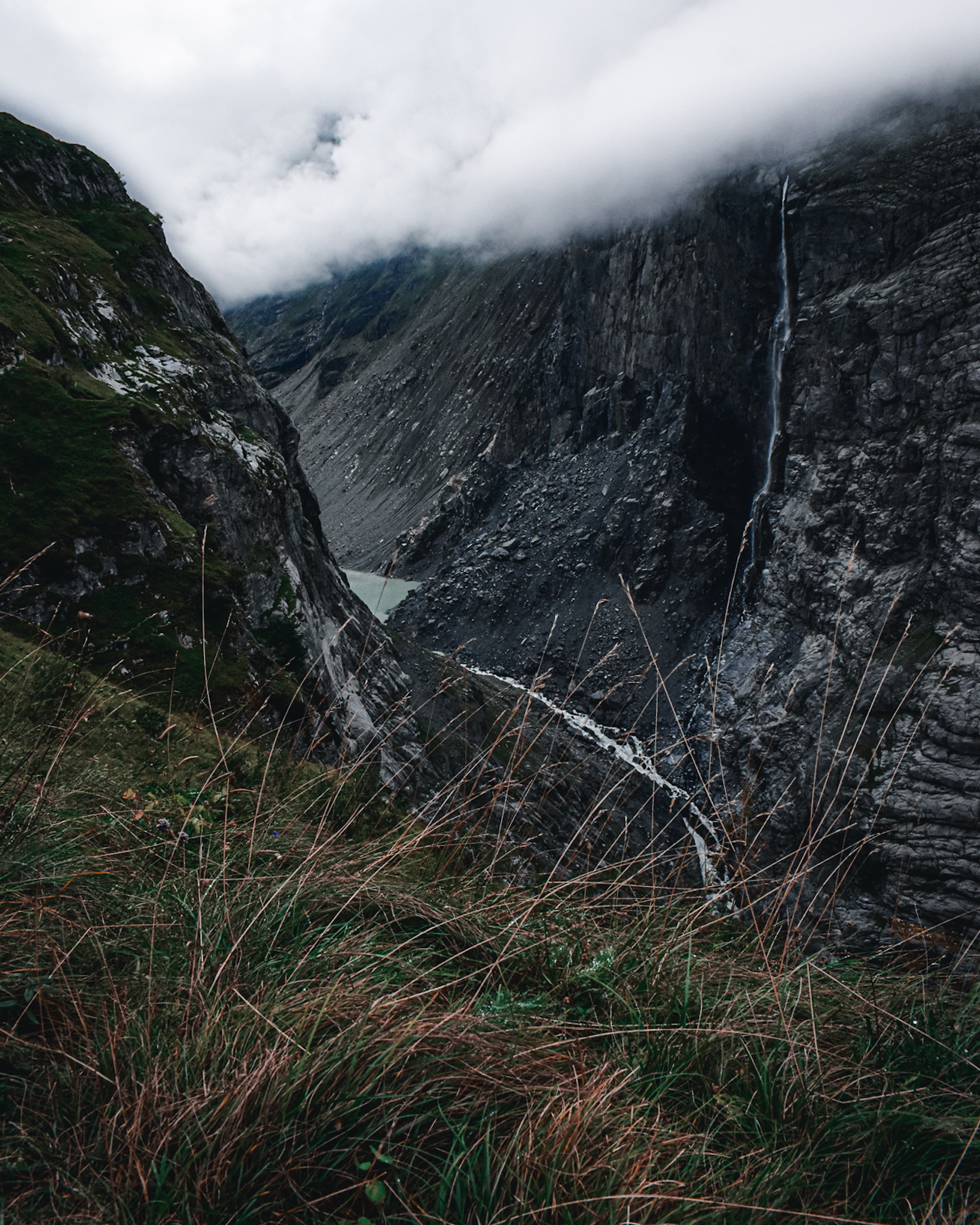 A tall waterfall in a mountain valley with clouds overhead as seen during a hut to hut hike in Switzerland