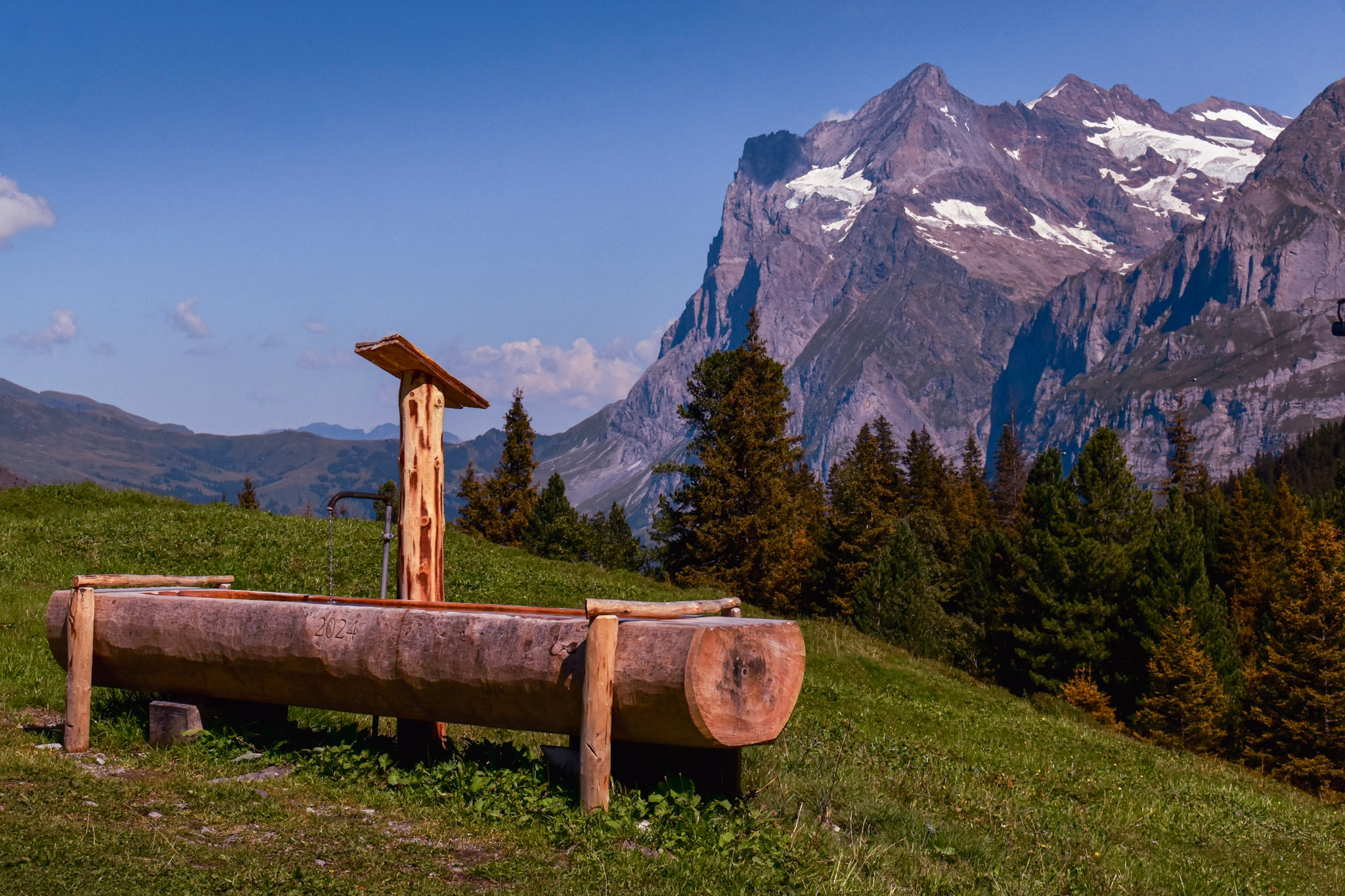 a natural wooden water fountain spring in switzerland with a mountain behind it