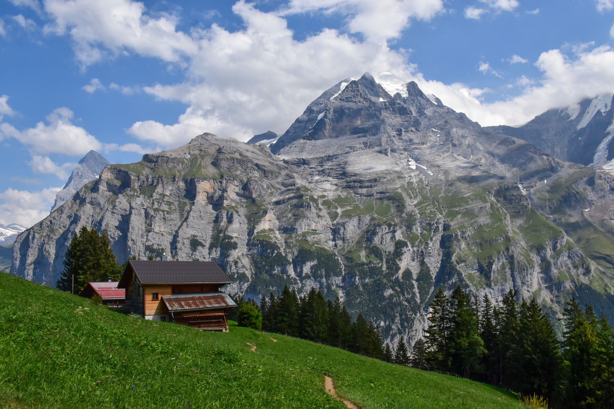 A swiss barn on a green pasture with a massive mountain behind it