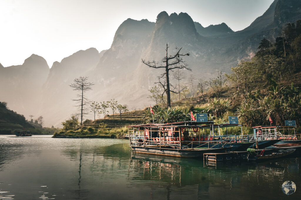 a boat rests in a still river below the ha giang mountains at sunrise