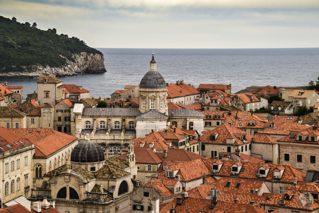 A chirch spire peaks above red tiled roofs in dubrovnik's old town, a must do